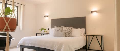 A modern bedroom with a large bed, two bedside tables, a hanging plant, and a black chair.