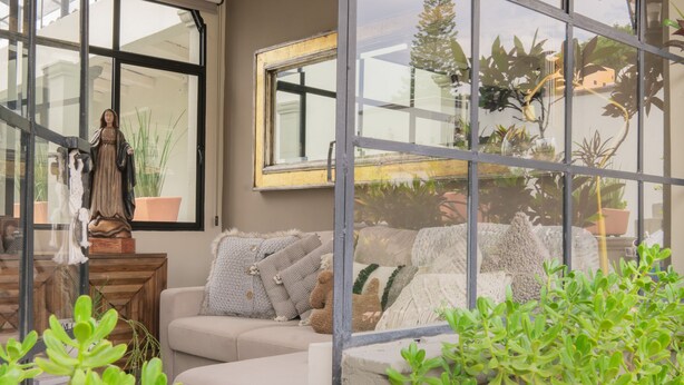 A cozy living room with a sofa, cushions, and a statue. There are potted plants and a window with a view of greenery. - Casa Doper Guadiana (San Miguel de Allende)