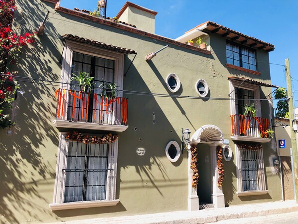 Un edificio con varios balcones, cada uno adornado con plantas en macetas y listones anaranjados.