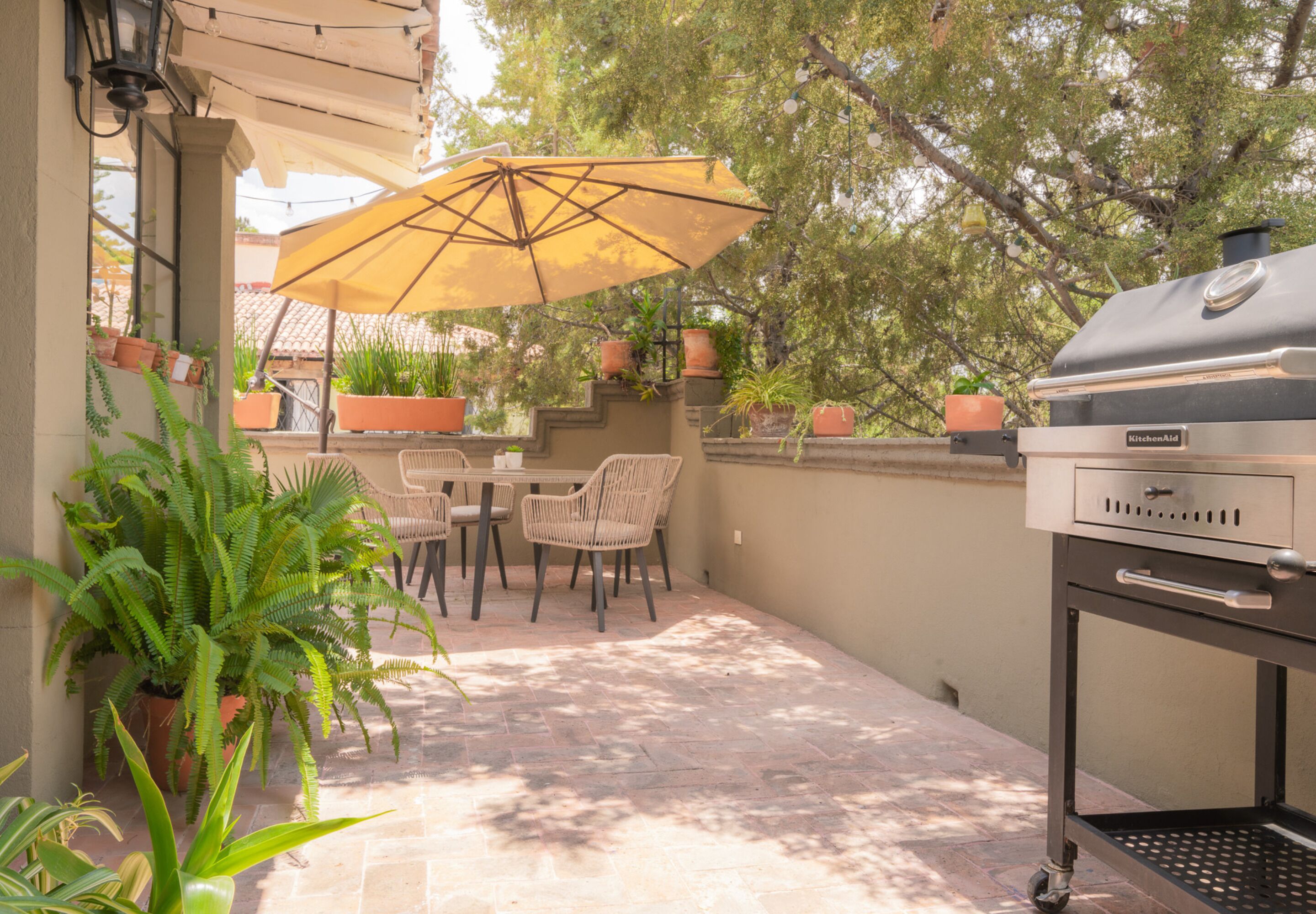An outdoor patio with a grill, chairs, and potted plants.