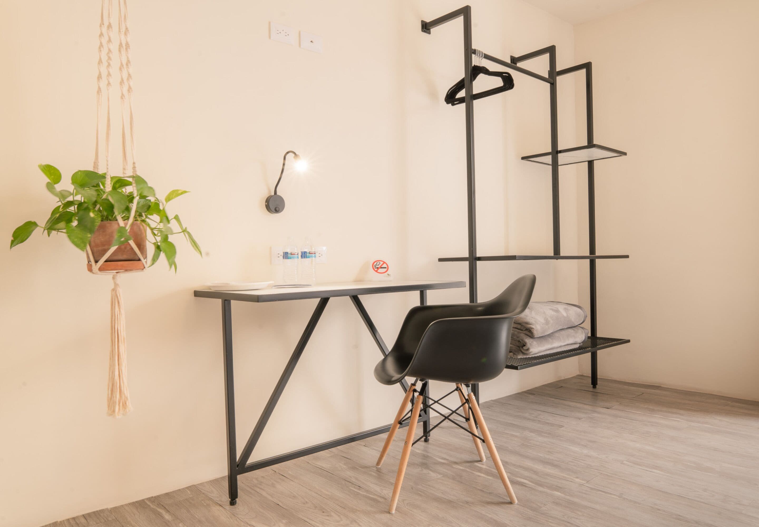 Una habitación moderna con un escritorio, una planta colgante, una silla y una estantería metálica negra.