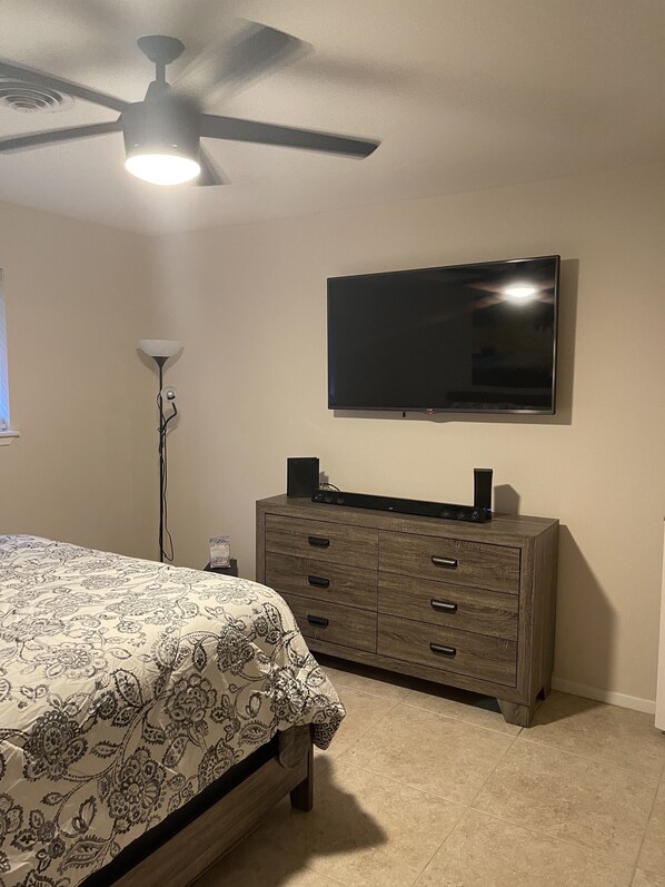 A bedroom with a bed, dresser, TV, ceiling fan, and floor lamp.