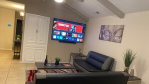En stue med et fladskærms-tv, der viser en film, en sofa, et sofabord og et lille sidebord.