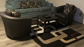 En stue med sofa, lænestol, sofabord og et tæppe.