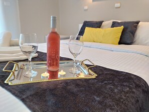 A bed with a dark grey blanket, a bedside table with a tray holding a bottle and two glasses, and a yellow pillow on the bed. - Modern Quiet Apartment in Rhodes center (Rhodes)