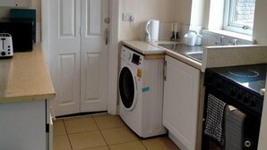Une cuisine compacte équipée d’un lave-linge, d’une cuisinière et d’une fenêtre laissant entrer la lumière naturelle.