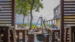 An outdoor dining area with wooden tables and chairs, a hanging light fixture, and a view of the sea. - Holiday apartment with lake view and balcony (Dramalj)