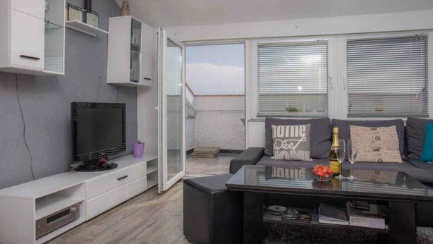 A modern living room with a flat-screen TV, a glass coffee table, a sofa with decorative pillows, and a sliding glass door leading to an outdoor area. - Holiday apartment with lake view and balcony (Dramalj)