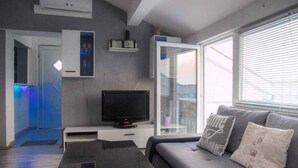 Ein modernes Wohnzimmer mit Fernseher, grauem Sofa und Glastür zum Balkon.