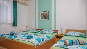 A room with two beds, a window with curtains, an air conditioner, and a framed picture on the wall.