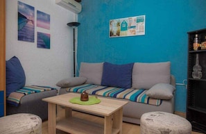 Un salón acogedor con sofá, otomanas, una mesa de centro y cuadros en la pared.