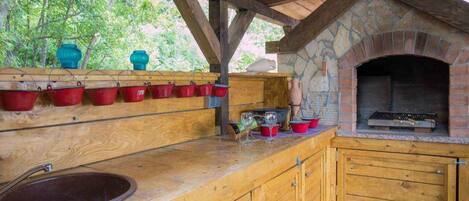 Une cuisine extérieure rustique avec un four en pierre, des armoires en bois et un évier.