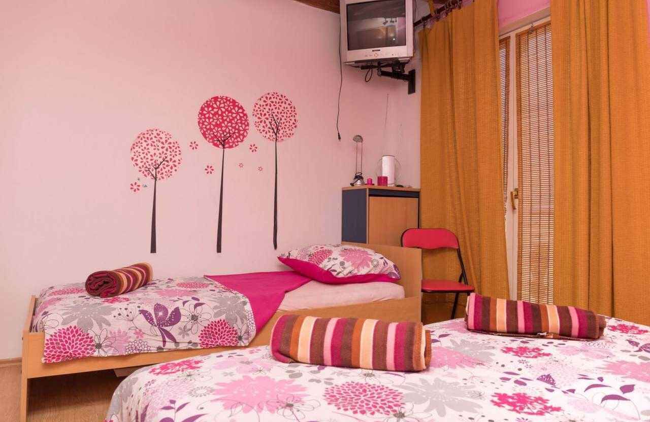 Een slaapkamer met twee bedden, een aan de muur bevestigde televisie, een bureau en een stoel.