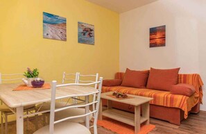 A room with a yellow wall, a sofa, a dining table with chairs, and two paintings. - Holiday apartment with air conditioning and roof terrace (Dramalj)