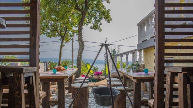An outdoor dining area with wooden tables and chairs, a hanging light fixture, and a view of the sea. - Holiday apartment with terrace and air conditioning (Dramalj)