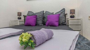 A neatly made bed with a purple towel and a small plant, two nightstands with lamps, and a wall-mounted picture. - Holiday apartment with terrace and air conditioning (Dramalj)