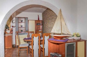 A dining area with a wooden table and chairs, a sailboat model, and a kitchen in the background.