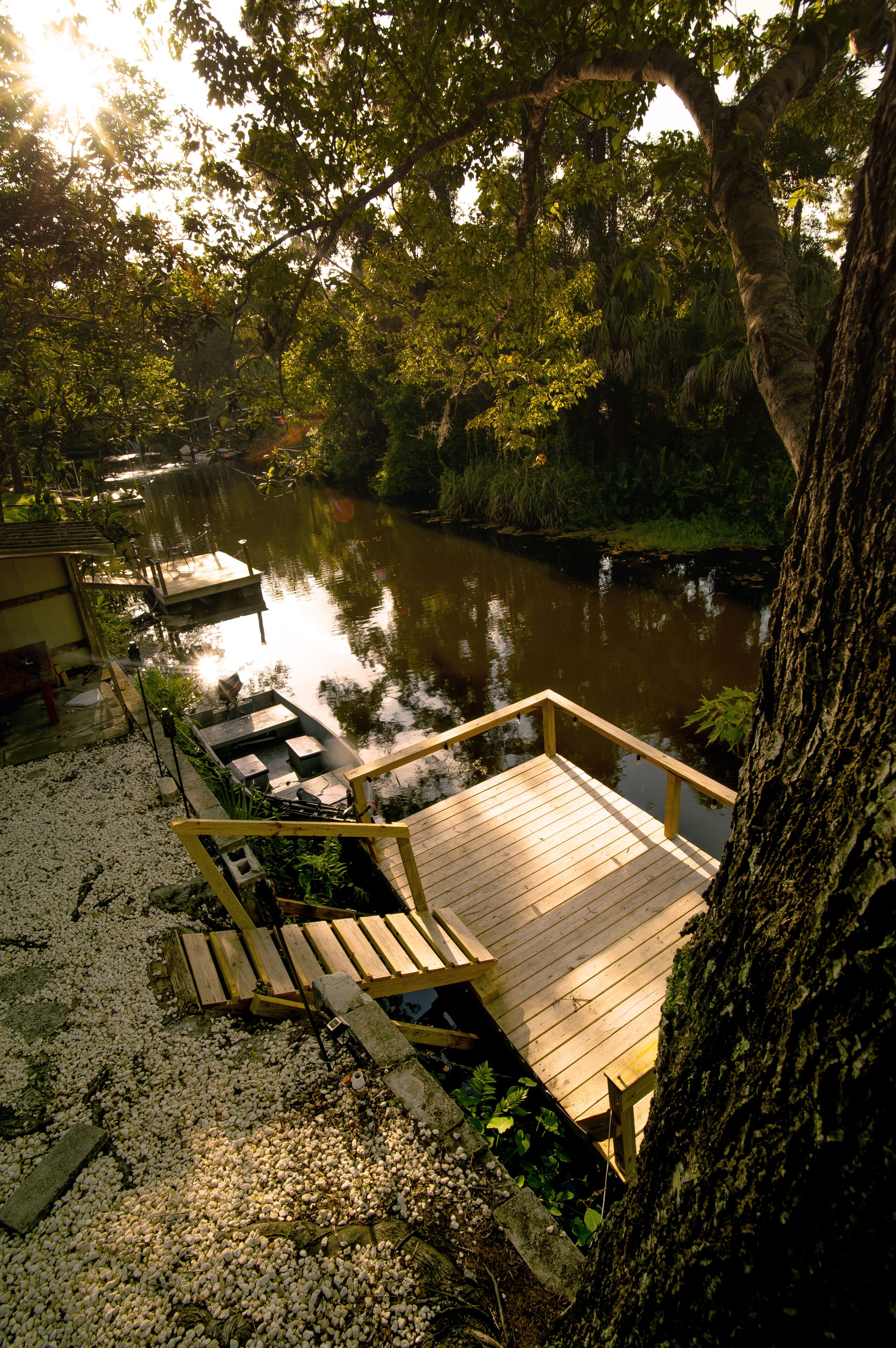 A wooden deck with a view of a calm river, surrounded by trees and vegetation.