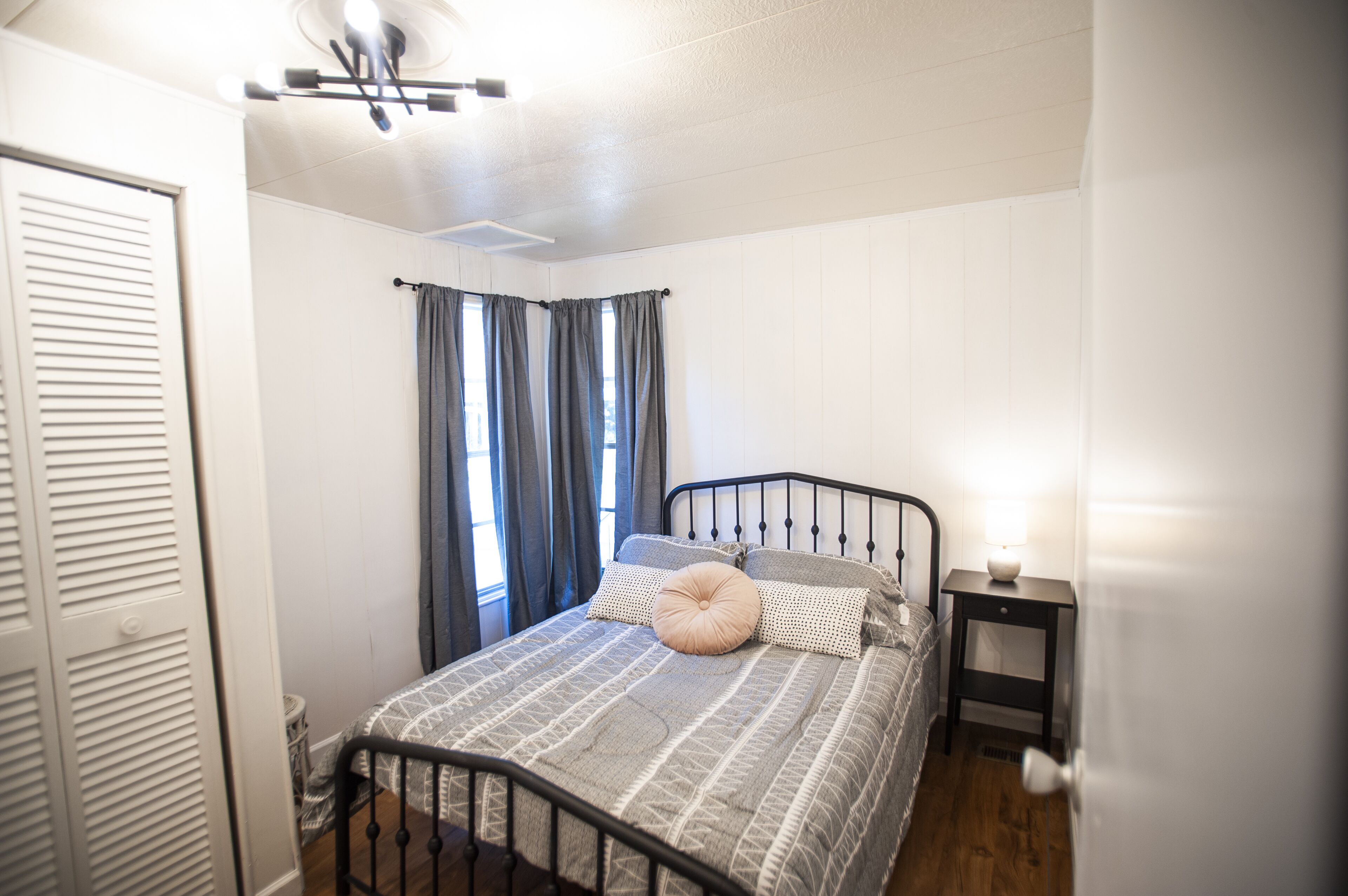 Un dormitorio con una cama, una mesita de noche, un ventilador de techo y una ventana con cortinas.