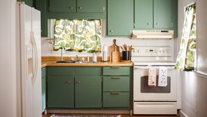 Una cucina con mobili verdi, un frigorifero bianco, un piano di lavoro in legno e una stufa bianca.