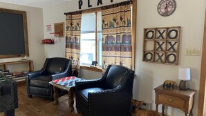 Un salon chaleureux avec deux fauteuils en cuir, un baby-foot et une fenêtre ornée d’un rideau à motifs de cerfs.