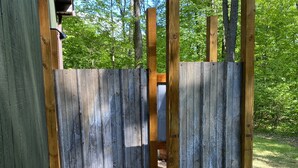 Une terrasse en bois, agrémentée d’une porte en métal, entourée d’arbres et de gravier.