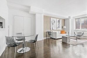 A modern living room with a glass dining table, two chairs, a white sofa, a grey armchair, and a coffee table. - Upper East Side Escape | Pet-Friendly, Laundry (New York)