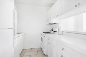 A compact kitchen with white cabinetry, a built-in microwave, a kettle, and a stove. - Upper East Side Escape | Pet-Friendly, Laundry (New York)
