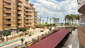Un edificio de varios pisos con balcones, una zona de estacionamiento techada y vistas a palmeras y una masa de agua.