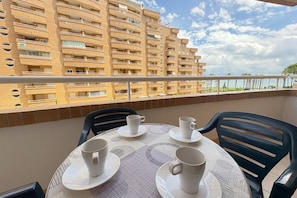 A balcony with a table set for four, overlooking a high-rise building and a clear sky.