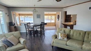 A spacious living room with a green sofa, a dining table with chairs, and a view of the outdoors. - Lake Front home with with pontoon boat available for rent (Marcellus)
