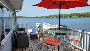 A deck with wicker furniture, a red umbrella, and a view of a lake. - Lake Front home with with pontoon boat available for rent (Marcellus)