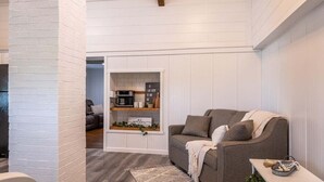 Een moderne woonkamer met een bank, een salontafel, en een keuken die zichtbaar is door een open deur.