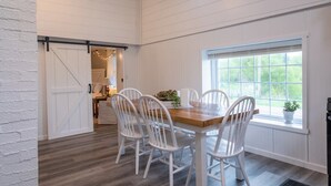 Een eetruimte met een houten tafel en witte stoelen, een raam met uitzicht en een schuifdeur in boerderijstijl.
