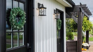 Een gebouw met zwarte deuren, een witte gevel en een houten pergola met beplanting.