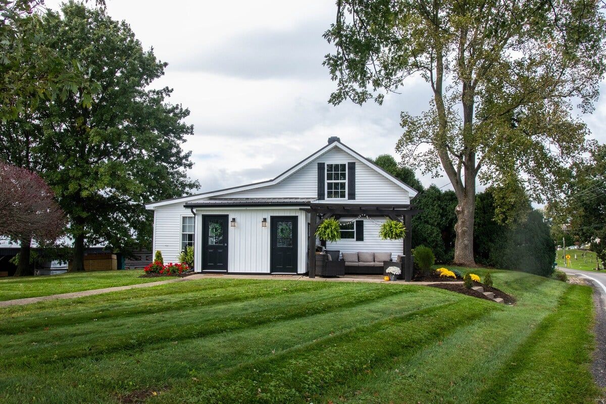 A single-story house with a front porch, a lawn, and a large tree to the right.