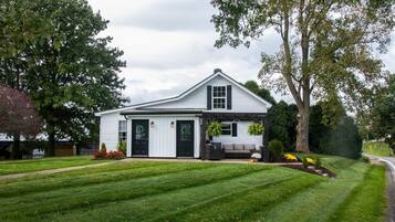 A single-story house with a front porch, a lawn, and a large tree to the right.