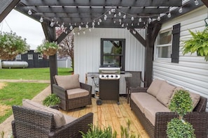 Eine überdachte Terrasse mit Korbmöbeln, einem Grill und Lichterketten.