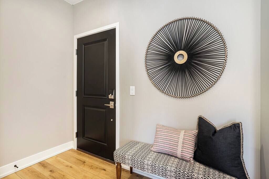 A room with a black door, a round wall decoration, and a bench with patterned cushions.