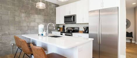 A modern kitchen with white cabinets, stainless steel appliances, and a central island with bar stools.