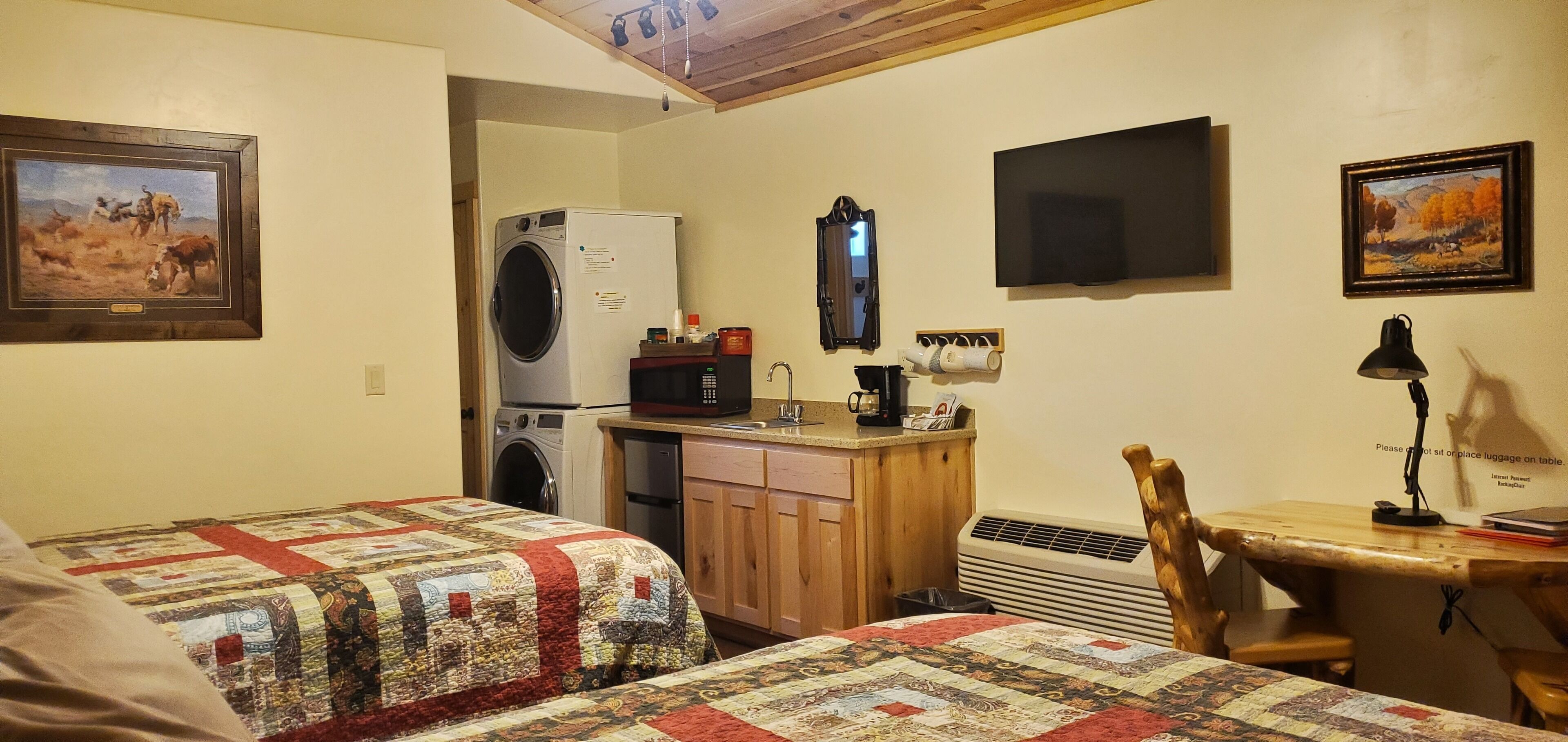 A small, cozy room with two beds, a washing machine, a microwave, a sink, and a desk with a chair.