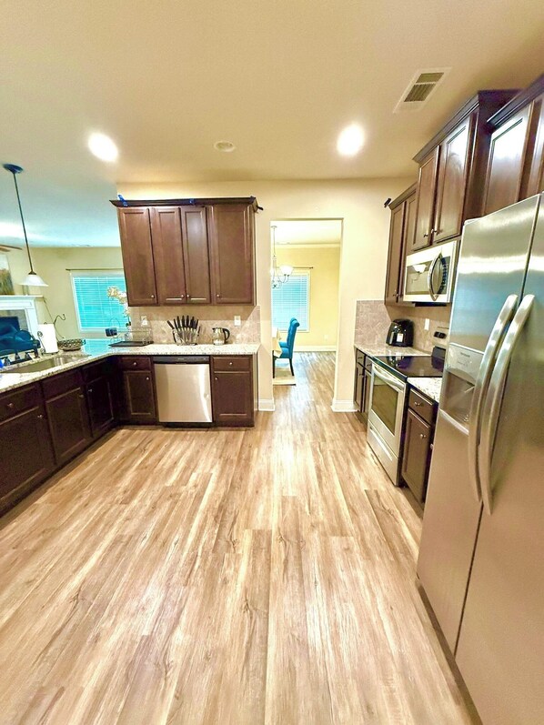 A modern kitchen with wooden cabinets, stainless steel appliances, and a wooden floor. - Beautiful New Cozy Home in a Gated Community (Hampton)