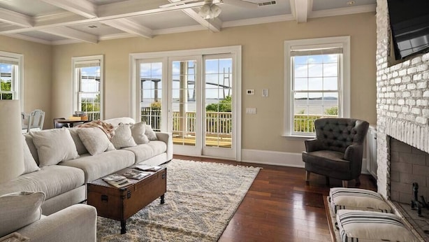 A spacious living room with a sofa, armchair, and fireplace, large windows, and a ceiling fan. - ☀️Picturesque Views💥Game room👙Pool & Hot Tub (Brunswick)