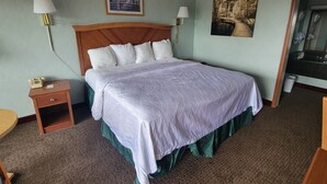 Habitación de hotel con una cama grande, dos lámparas de noche, una mesita de noche pequeña con un teléfono, un cuadro enmarcado sobre la cama y un espejo en la esquina.