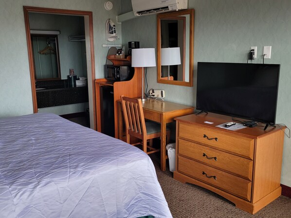 A hotel room with a bed, a desk with a chair, a television, and a dresser.
