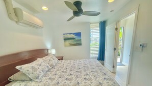 Ein Schlafzimmer mit Bett, Deckenventilator, einem Gemälde und Blick ins Freie.