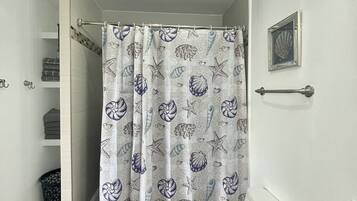 Une salle de bain avec un rideau de douche orné d’un motif représentant des coquillages et des étoiles de mer, des toilettes, un porte-serviettes et un tableau encadré accroché au mur.