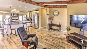 A spacious living room with a large TV, wooden flooring, and a kitchen in the background. - New!!! Amazing river and mountain deck view home!!!! (Parker)