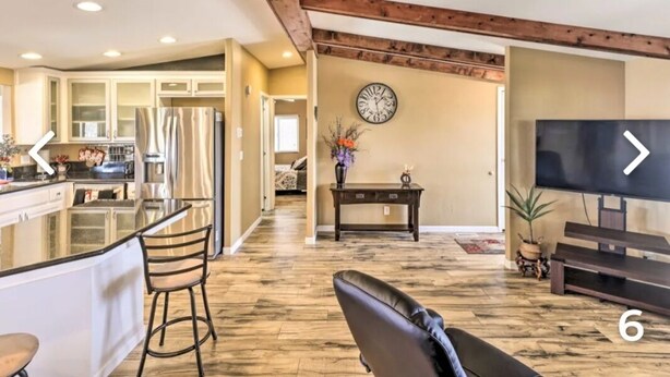 A spacious living area with a large TV, wooden flooring, and a kitchen in the background. - New!!! Amazing river and mountain deck view home!!!! (Parker)
