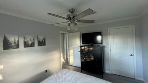Un dormitorio con cama, cómoda, televisor y ventilador de techo.